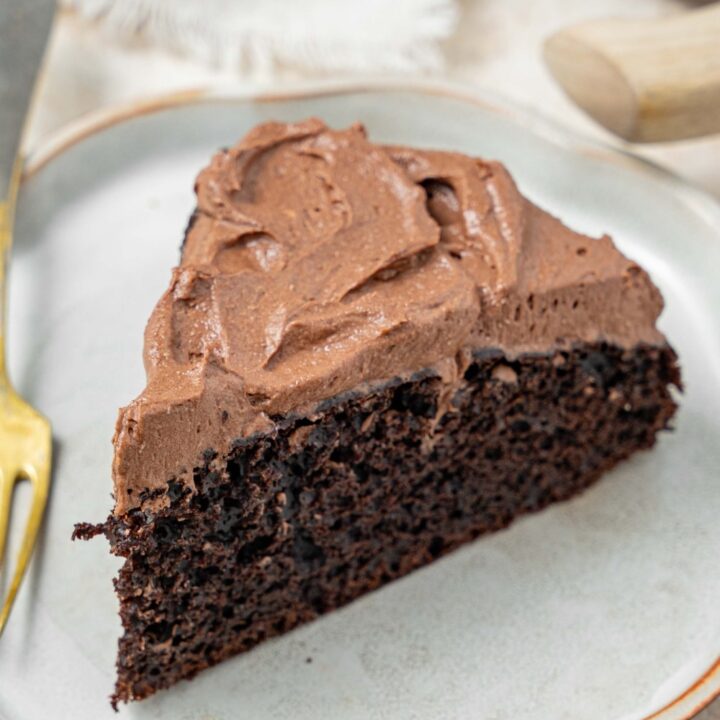 A slice of chocolate cake topped with chocolate frosting on a plate with a fork.