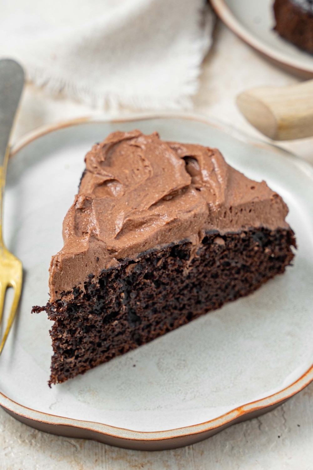 A slice of chocolate cake topped with chocolate frosting on a plate with a fork.