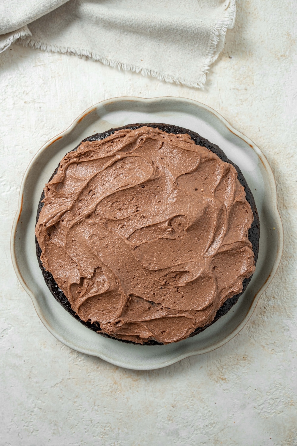 Overhead view of a chocolate cake covered in chocolate frosting on a serving plate.