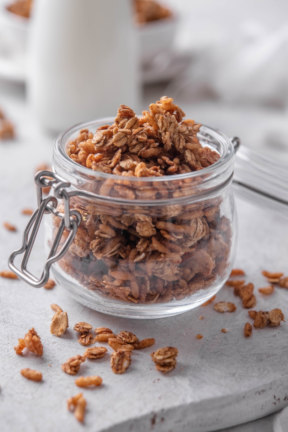 A clear jar filled with granola with pieces of granola spilling over the jar onto the counter.