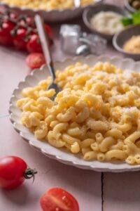 A plate of mac and cheese topped with grated cheese. There is a fork on the plate.