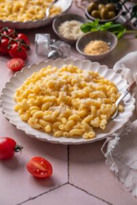 A plate of mac and cheese topped with grated cheese. There is a fork on the plate.