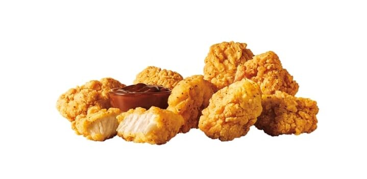 Several pieces of Sonic jumbo popcorn chicken with a cup of dipping sauce on a white background.