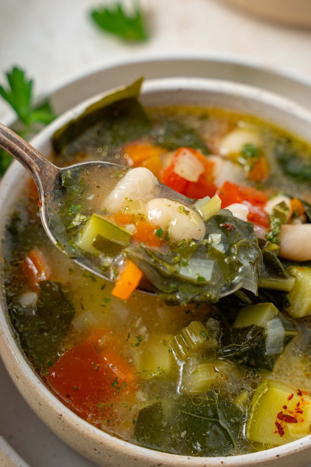 A close up of spoon scooping into vegetable weight loss soup. The soup is in a ceramic bowl on a ceramic plate.