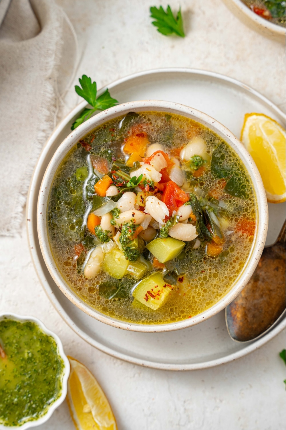 An overhead shot of vegetable weight loss soup in a ceramic bowl on a ceramic plate. There is a spoon and lemon wedge to the side of the bowl.