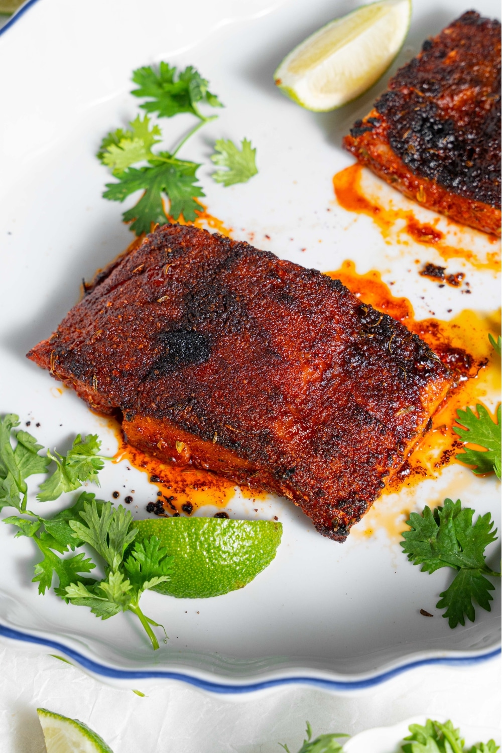 A piece of cooked blackened mahi mahi on a baking dish garnished with sprigs of parsley and a lime wedge. There is a second piece of cooked blackened mahi mahi in the baking dish.