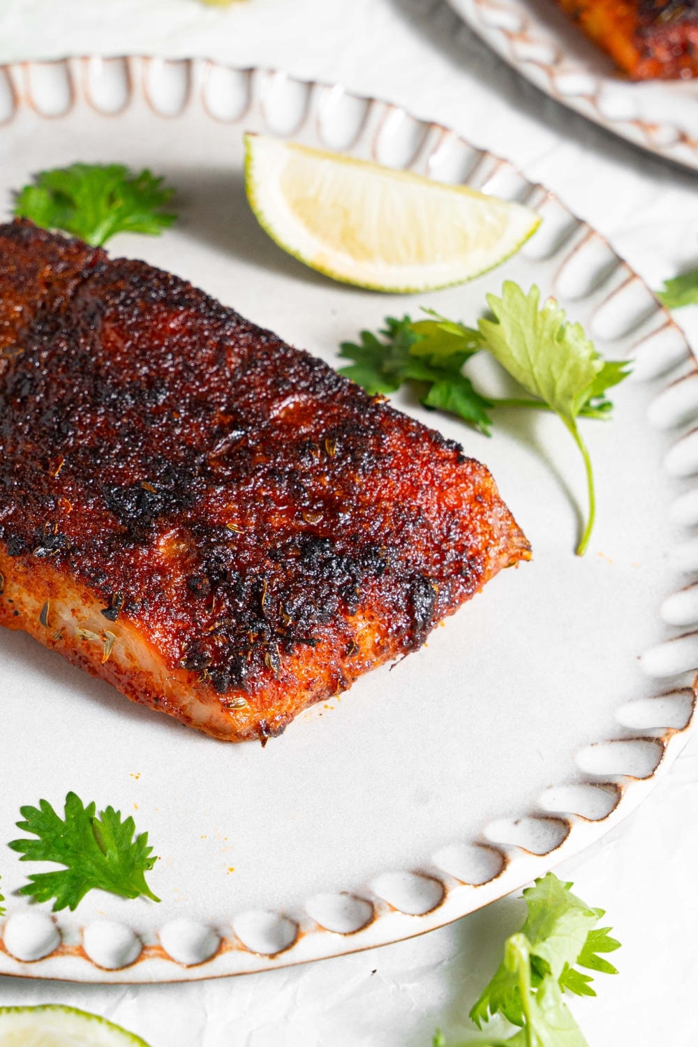 A close up of blackened mahi mahi on a ceramic plate on top of a marble counter. The plate is garnished with parsley and lime.