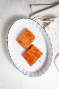 An overhead shot of a baking dish with two raw seasoned mahi mahi fillets. The baking dish is on a marble counter with a cloth napkin next to it.