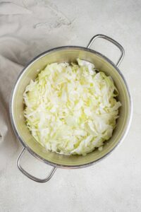 An overhead shot of a large pot filled with steamed cabbage. The pot is on a marble counter with a cloth napkin off to the side.