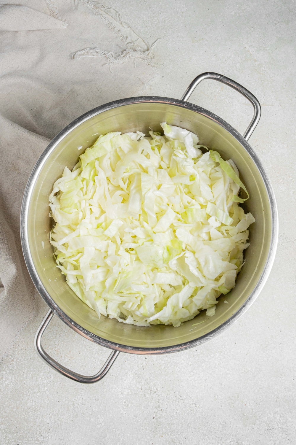 An overhead shot of a large pot filled with steamed cabbage. The pot is on a marble counter with a cloth napkin off to the side.
