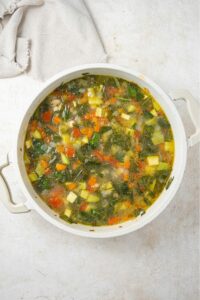 An overhead shot of a stock pot filled with vegetable weight loss soup on a marble counter and a cloth napkin on the side.