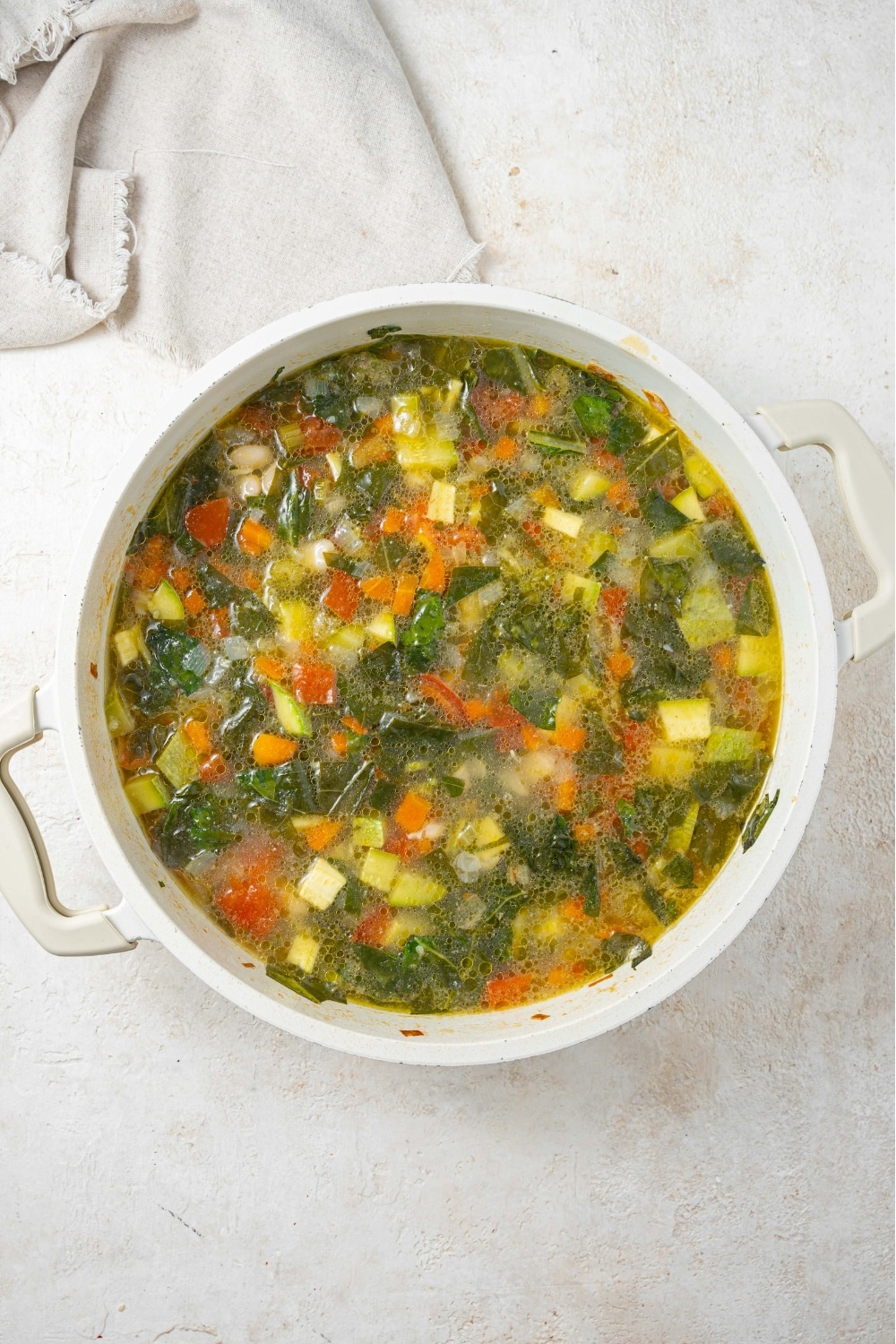 An overhead shot of a stock pot filled with vegetable weight loss soup on a marble counter and a cloth napkin on the side.