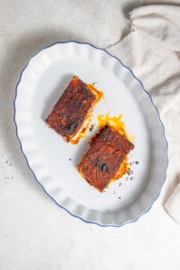 An overhead shot of a baking dish with two cooked blackened mahi mahi fillets. The dish is on a marble counter with a cloth napkin next to it.