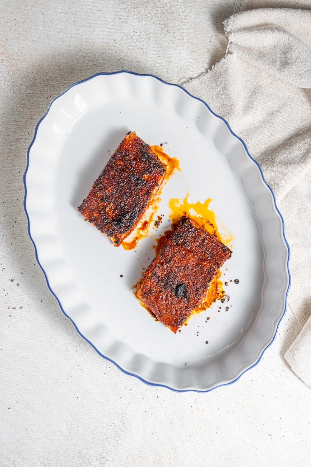An overhead shot of a baking dish with two cooked blackened mahi mahi fillets. The dish is on a marble counter with a cloth napkin next to it.