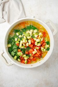 An overhead shot of a large stock pot with chopped veggies over a chicken stock mixture on a marble counter with a cloth napkin on the side.