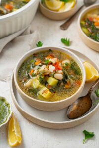A bowl of vegetable weight loss soup in a ceramic bowl on a ceramic plate. There is a spoon and lemon wedge on the plate with an additional bowl of soup next to the plate.