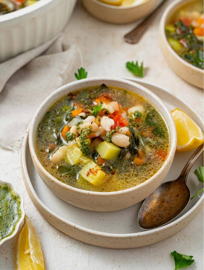 A bowl of vegetable weight loss soup in a ceramic bowl on a ceramic plate. There is a spoon and lemon wedge on the plate with an additional bowl of soup next to the plate.
