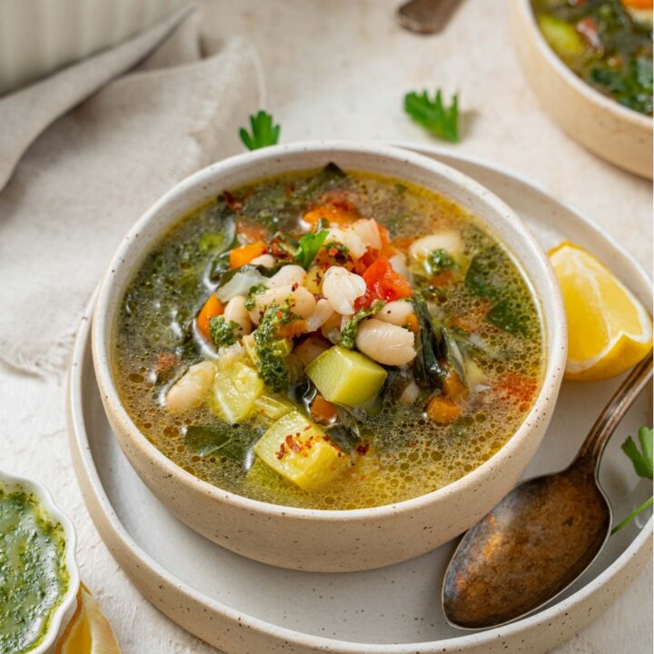 A bowl of vegetable weight loss soup in a ceramic bowl on a ceramic plate. There is a spoon and lemon wedge on the plate with an additional bowl of soup next to the plate.