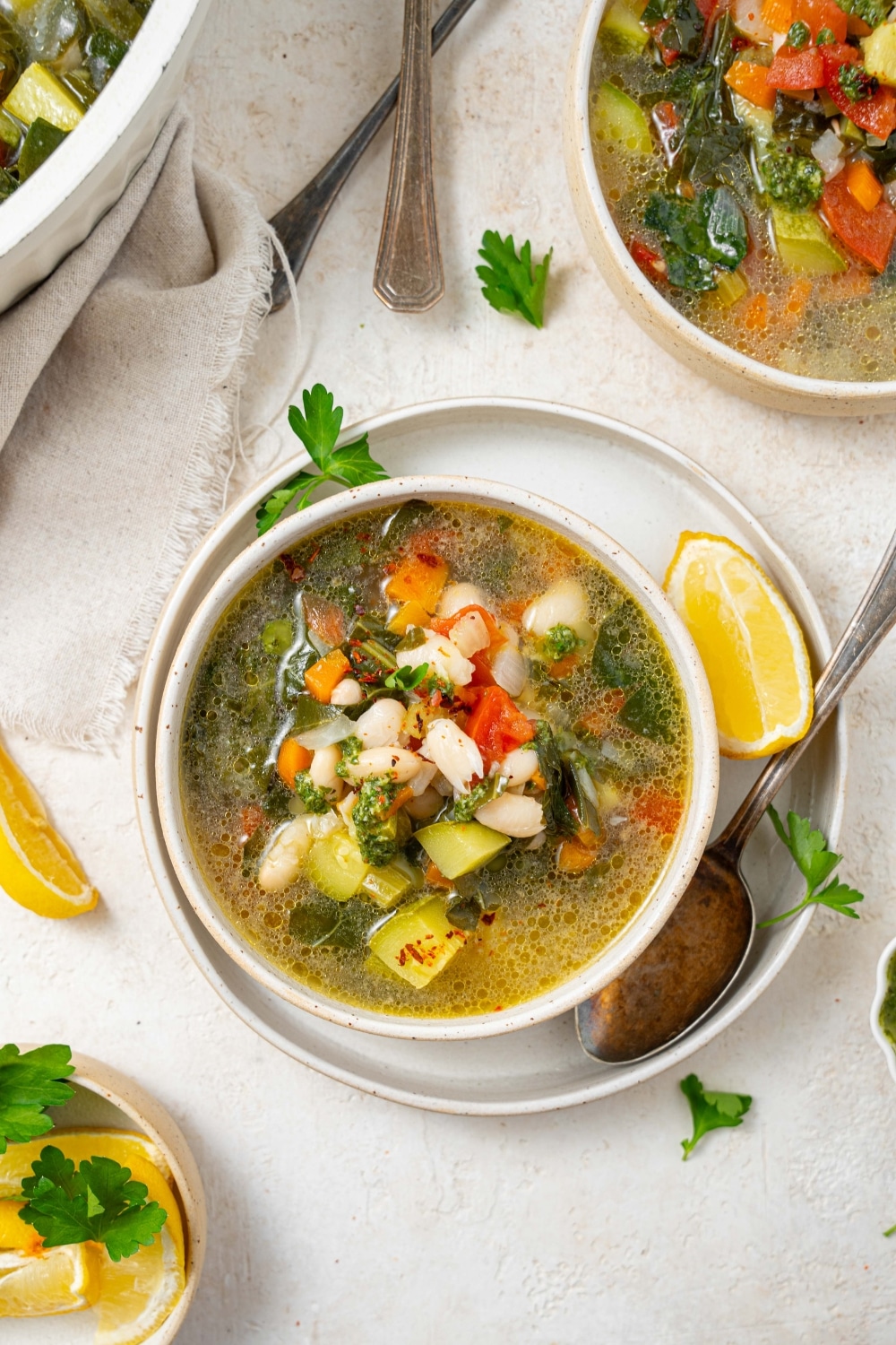 An overhead shot of vegetable weight loss soup in a ceramic bowl on a ceramic plate. There is a spoon and lemon wedge on the plate with an additional bowl of soup next to the plate.