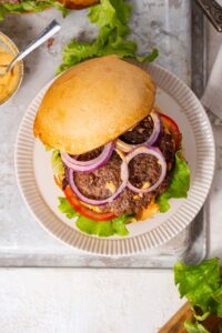 A semi-open smash burger, revealing red onion slices and burger sauce layered on top of a smash burger patty with vegetables.