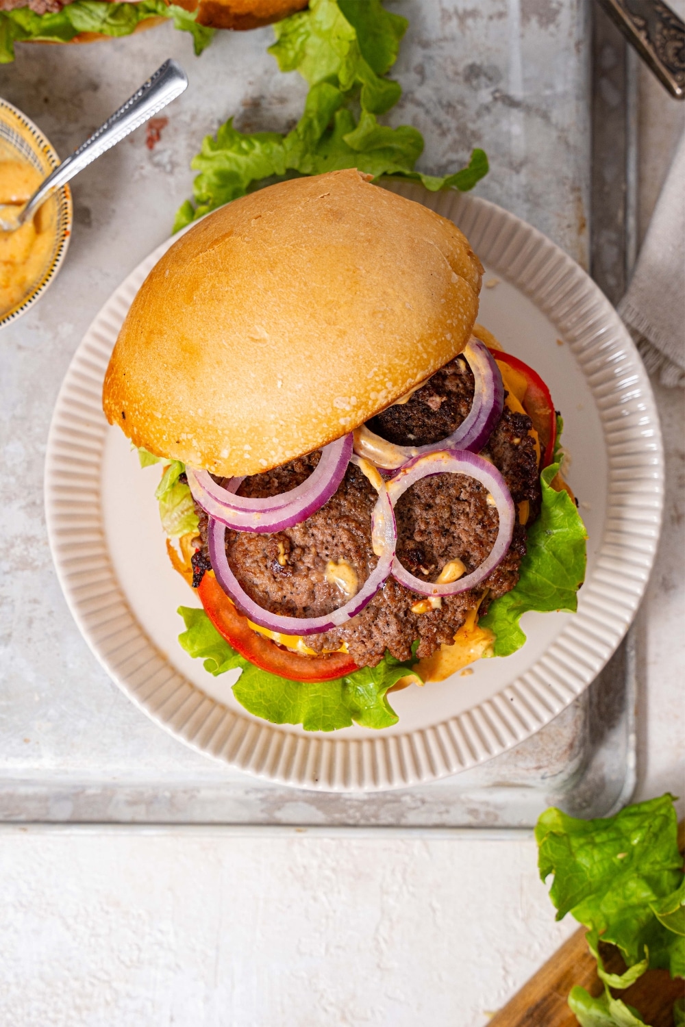 A semi-open smash burger, revealing red onion slices and burger sauce layered on top of a smash burger patty with vegetables.