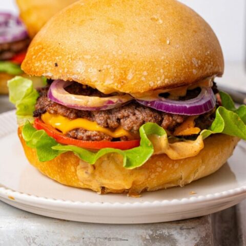 A smash burger filled with smashed burger patties, cheese, red onion slices, tomato slices, lettuce, and burger sauce.