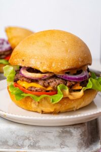 A smash burger filled with smashed burger patties, cheese, red onion slices, tomato slices, lettuce, and burger sauce.