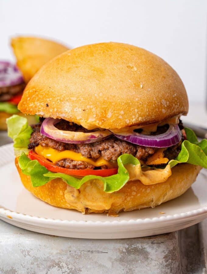 A smash burger filled with smashed burger patties, cheese, red onion slices, tomato slices, lettuce, and burger sauce.