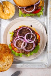Top view of an open smash burger, featuring red onion slices on a smashed burger patty.