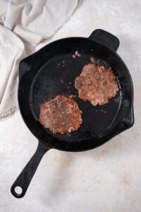 Two smashed burger patties in a skillet.