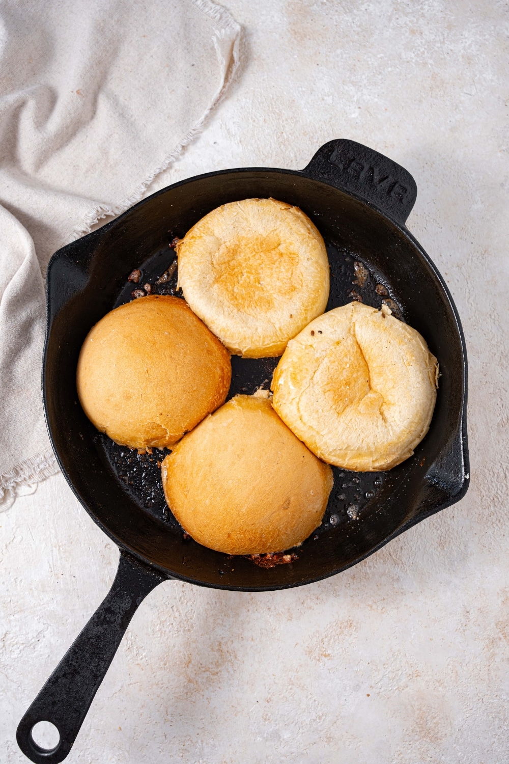 Four burger buns in a cast iron skillet.