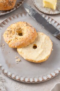 A cottage cheese bagel with everything bagel seasoning and butter spread. The bagel is on a grey ceramic plate with a knife to the side.