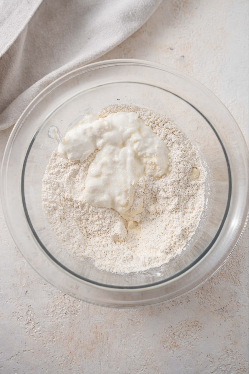 An overhead shot of a glass bowl with a cottage cheese flour mixture on a marble counter.