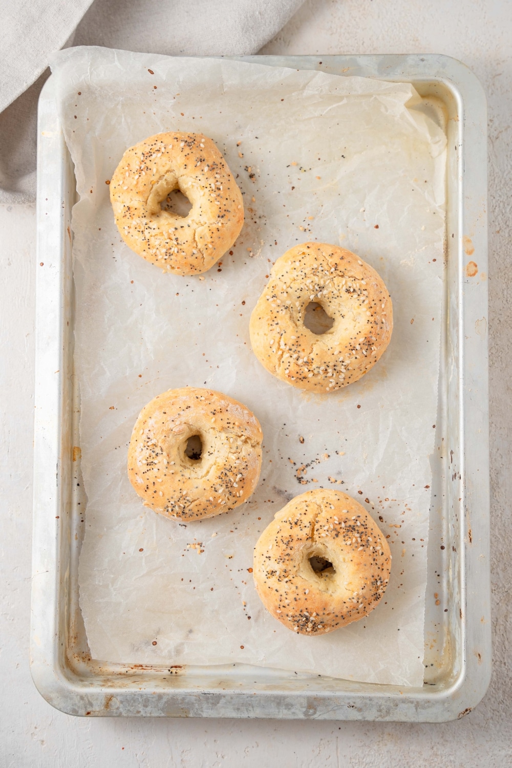 An overhead shot of a baking sheet lined with parchment paper. There are four cooked cottage cheese bagels seasoned with everything bagel seasoning on the baking sheet.