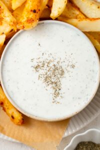 Cottage cheese ranch dip in a bowl, garnished with dry herbs and served with seasoned french fries.