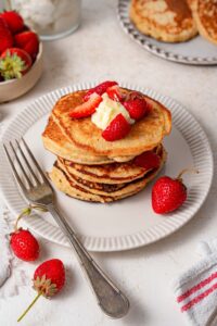 A stack of cottage cheese pancakes topped with butter and strawberries.