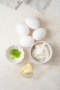 Four eggs and small bowls of cottage cheese, chives, and butter.