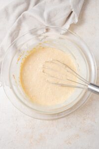 Whisked cottage cheese pancake batter in a glass bowl with a whisk.