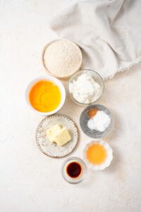 Bowls of cottage cheese, eggs, agave syrup, vanilla extract, oat flour, cinnamon, baking powder, salt, and butter.