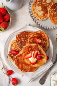 Cottage cheese pancakes arranged on a plate and garnished with butter and strawberries slices.