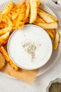 Cottage cheese ranch dip served in a bowl with a plate of seasoned french fries.