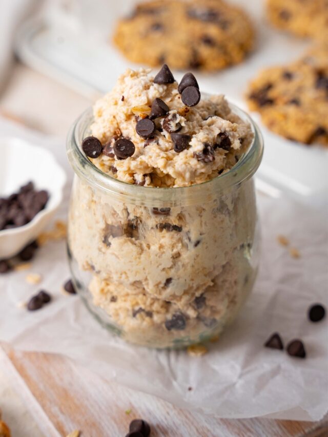 Cottage cheese chocolate chip cookie dough in a glass pot, in front of a tray of chocolate chip cookies.