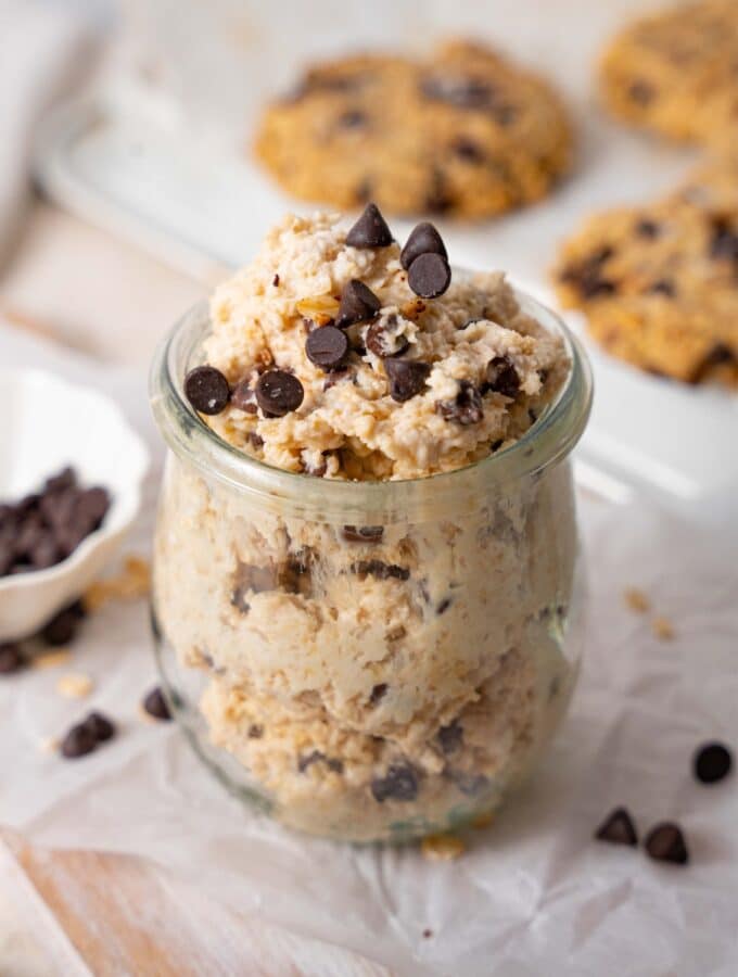 Cottage cheese chocolate chip cookie dough in a glass pot, in front of a tray of chocolate chip cookies.