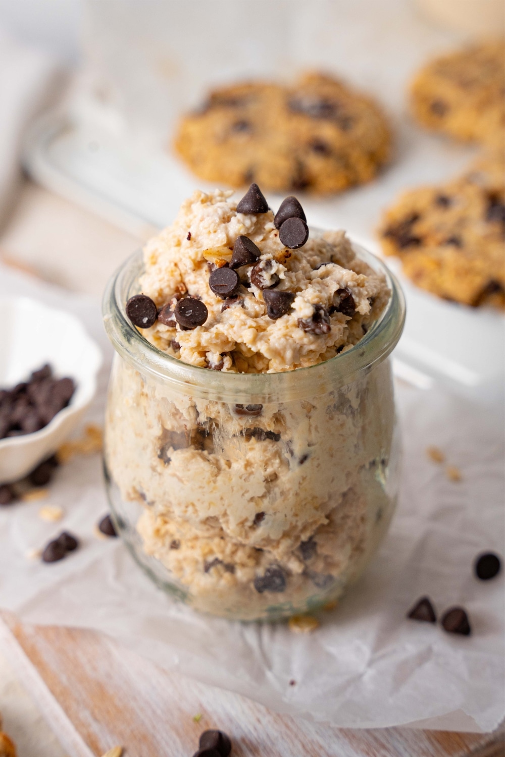 Cottage cheese chocolate chip cookie dough in a glass pot, in front of a tray of chocolate chip cookies.