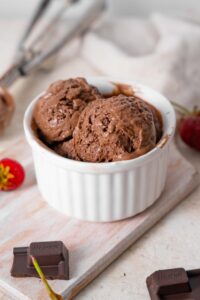 Chocolate cottage cheese ice cream in a ramekin, surrounded by strawberries and chocolate bar bits.
