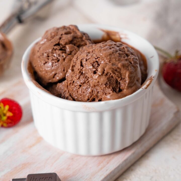 Chocolate cottage cheese ice cream in a ramekin, surrounded by strawberries and chocolate bar bits.