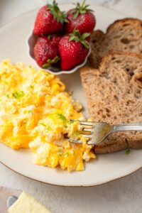 A fork digging into a cottage cheese omelet served with strawberries and toasted whole wheat bread slices.