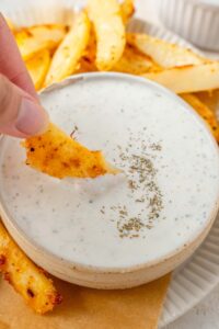 Dipping a seasoned french fry into a bowl of cottage cheese ranch dip.