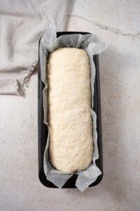 Uncooked bread dough in a bread pan lined with parchment paper.