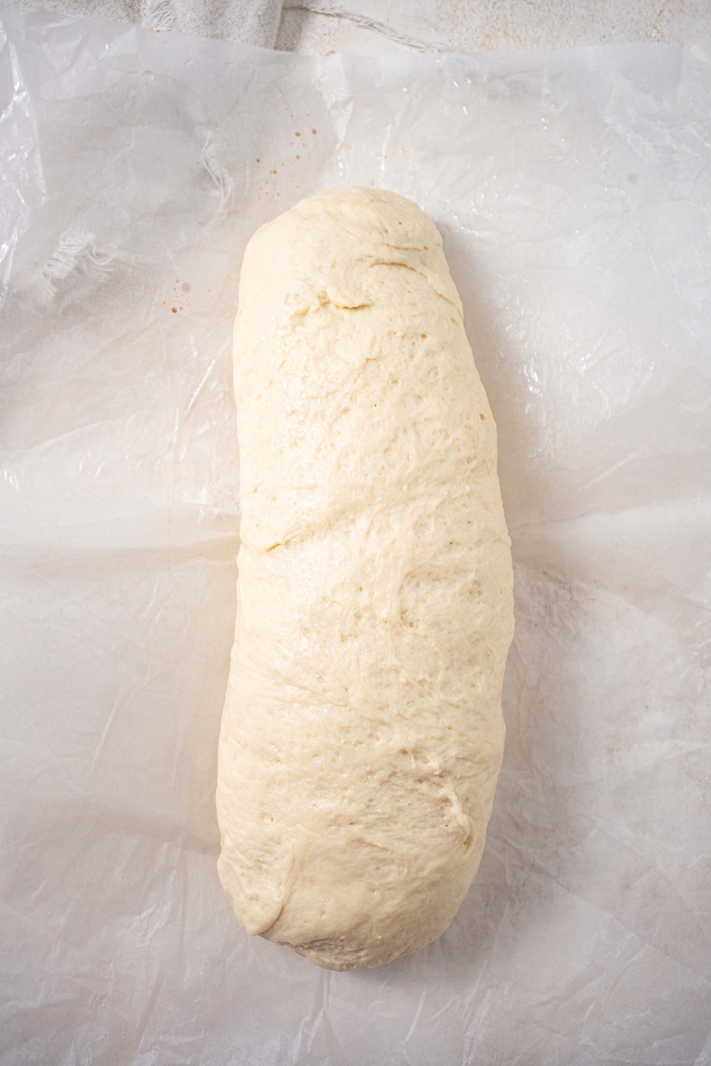 A roll of bread dough over parchment paper on a countertop.
